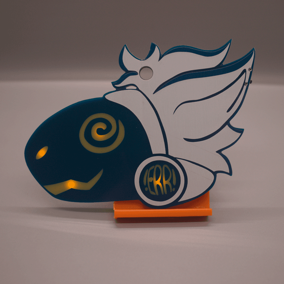 Photo of a PCB badge in the shape of a furry protogen's head. They have yellow facial features, white hair, ontop a blue base. Their eye is swirly, and the symbol on their cheek reads "!ERR!".