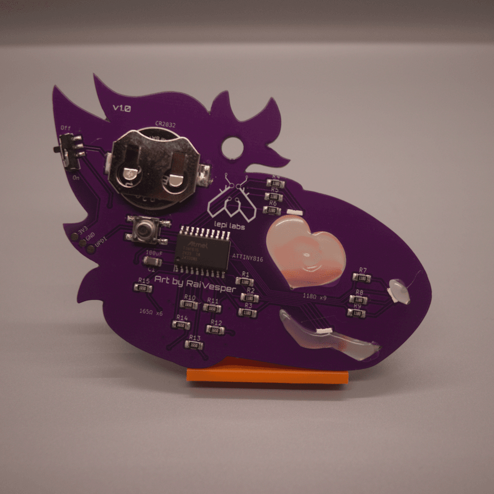 The back side of a purple PCB badge in the shape of protogen's head. They have a heart shaped eye, a nose, and a mouth which are all filled in with hot glue. The components are shown, including a coin cell battery, a microcontroller, resistors, RGB LEDs near the glue, a push button mode switch, a sliding power switch, and a UPDI connector.